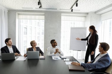 Modern ofis odasındaki çeşitli iş adamlarına eğitim dersi ya da atölye dersi veren çizelgeli çizelgelerle birlikte takım elbiseli kadın konuşmacı..