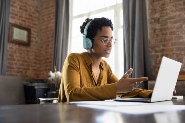 Kulaklıklı şık siyahi bir işçi, çalışma masasındaki kağıt dökümanlarda müşteriyle görüntülü konuşma yapmakla meşgul. İnternet 'te Webinar öğrenimi izleyen üniversite öğrencisi, online çalışıyor.