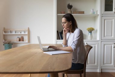 Gözlüklü genç bir kadın dizüstü bilgisayara bakıyor araştırma yapıyor internet kullanıyor, web sörfü bilgisi kullanıyor, ödev yapıyor ya da internetten kablosuz bilgisayar kullanıyor. Teknoloji, serbest çalışma kavramı