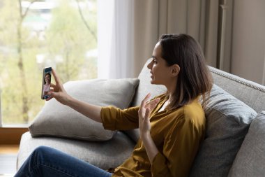 Kanepede oturan genç kadın cep telefonuyla en iyi kız arkadaşıyla yaptığı konuşmalara bakıyor video konferans uygulaması kullanıyor, planlarını paylaşıyor ve haberlerin mesafeli iletişiminin tadını çıkarıyor. Sanal toplantı, video çağrı etkinliği konsepti