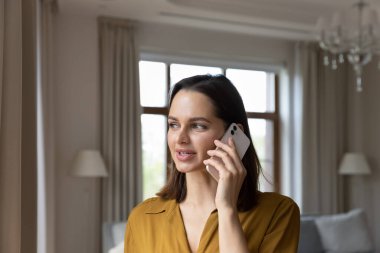 25 'li yaşlardaki çekici bir kadın lüks bir oturma odasında akıllı telefondan konuşuyor. Cep telefonu operatörü kullanımı, erkek arkadaşla hoş sohbetler, telefon görüşmesinde kişisel iletişim.