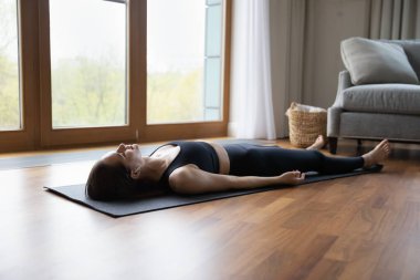 Paspasın üzerine uzanmış genç bir kadın kulaklıklarla meditasyon müziği dinliyor evde asana egzersizi yapıyor, Corpse Savasana Dead Body yapıyor, yoga eğitiminden sonra dinleniyor. Yeniden düzenle, iç dengeyi güçlendir, stres yok.