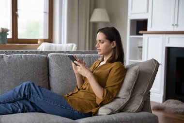 Yan bakış genç ciddi kadın koltukta oturur akıllı telefon mesajları atar, mesajlaşır, mesajlaşır arkadaşlarıyla internet üzerinden iletişim kurar. Hafta sonu boş vakit kullanımı modern kablosuz teknoloji, mobil uygulama kavramı