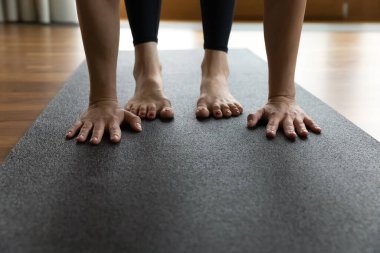 Siyah kauçuk paspasın üzerinde çıplak ayakla duran kadın Uttanasana egzersizi, kesilmiş vücut parçası görüntüsü, avuçlar ve ayaklar görüntüyü kapatıyor. Yoga asana, antrenman, spor sınıfı konsepti