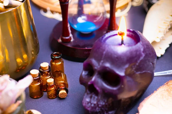 Selective focus on empty potion bottles. Occult and esoteric witch doctor still life. Halloween with magic objects. Black human skull candle, goat skull teeth on witch table. Mystic witchery macro.