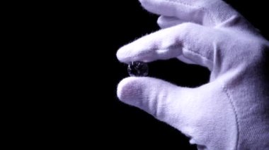 Beyaz eldivenli kuyumcu elleri lüks, parlak elmasın kalitesini inceler. Seçici odaklanma, makro. Değerli taş, yıldız ışınlarıyla parıldıyor. Nişan ya da alyans için yuvarlak elmas.