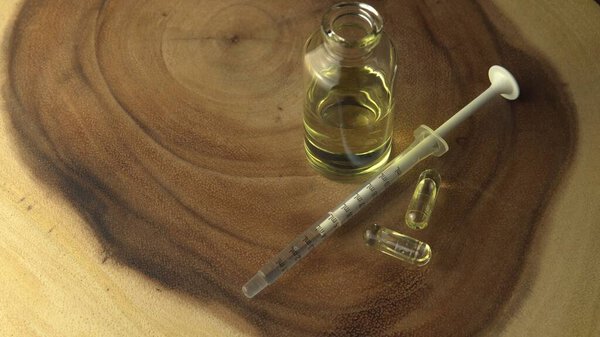 Very close view of CBD oil, oral syringe, pills for anxiety and stress relief near the glass jar on the wood circle tree ring table with ripple line pattern. Revolution in pain treatment and healing. 