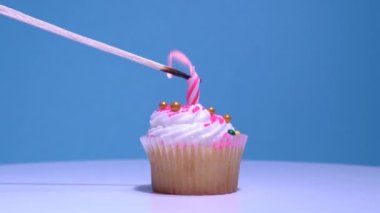 Kekin üzerine doğum günü mumu yakıyorum, yakın plan. Pembe arka planda yanan mum ile nefis bir fincan kek. Tereyağlı kremalı ev yapımı vanilyalı kek. Sığ alan derinliği.
