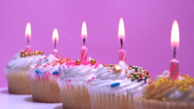 Doğum günü pastalarında mum yakmak. Ev yapımı kek ve pembe arka planda mumlardan alevler üflemek. Çocukların doğum günü partisi için tatlı. Yakın çekim, alan derinliği az..