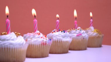 Turuncu arka plan rotasyonunda yanan mumları olan doğum günü kekleri. Krem şantili ve şekerli vanilyalı hindistan cevizli kek. Yakın çekim, alan derinliği az..