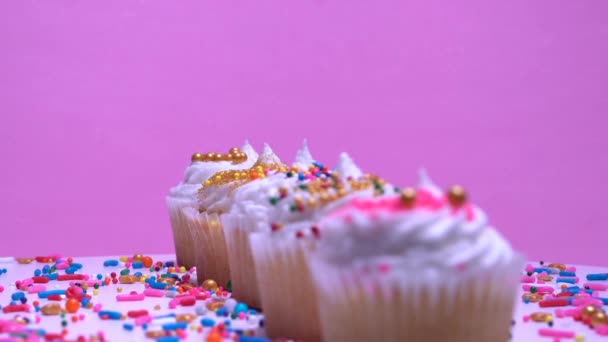 女性の手はカップケーキを飾ります フィールドフォーカスの浅い深さ マフィンに集中してください ピンクの背景 記念日や誕生日のデザートのプレゼンテーション — ストック動画