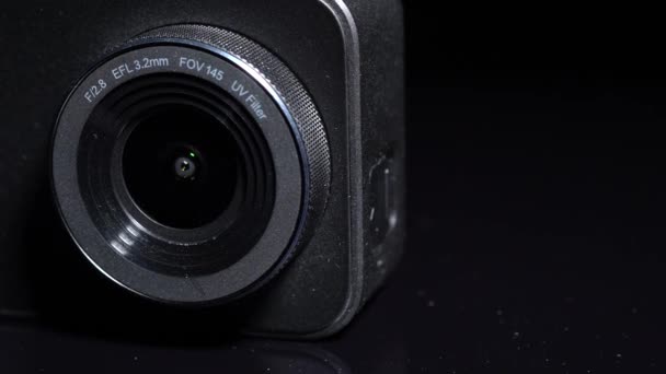 一般的な4Kアクションカメラマクロは 選択的なフォーカスを閉じます 黒の背景にシンプルな現代的な小型ビデオカメラレンズの回転 Vloggerのソーシャルメディアとインフルエンサーのカムの概念 — ストック動画