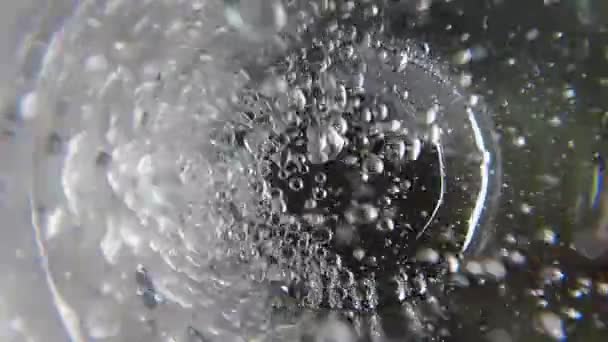 Botten av vattenglas. Vatten hälls i glas från kanna eller kanna slow motion. Super makro närbild selektivt fokus. Bubblor och vatten virvlar i glaset. Utsikt underifrån. — Stockvideo