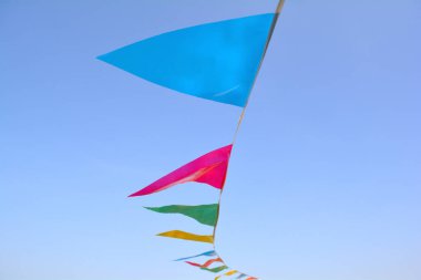 Üçgen bayrakları mavi gökyüzüne karşı ip asılı. Filtre uygulanmamış, doğal aydınlatma ile. Çok renkli kutlama parti üçgen bayrakları.