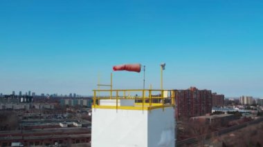 Arka planda mavi gökyüzü ve şehir olan Windsock. Rüzgar yönü ve hızı için konik tüp bayrağının yavaş hareketi. Havaalanlarında ve üretim tesislerinde kullanılır. Havadan.
