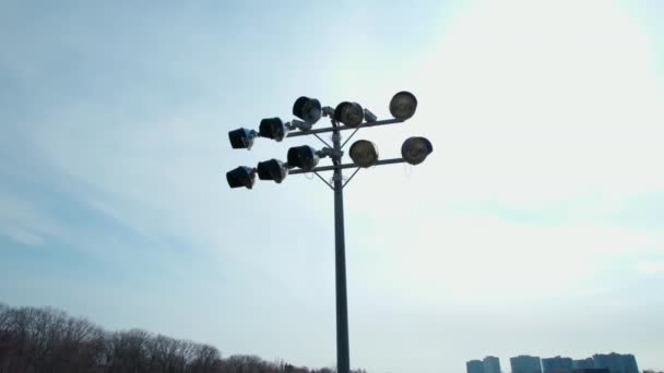 Aérea con torres de luz de un estadio de fútbol contra una puesta de sol y nubes de cielo azul, rotación cinematográfica y movimiento suave alrededor de las luces. Estadio de fútbol linternas de cerca. — Vídeo de stock