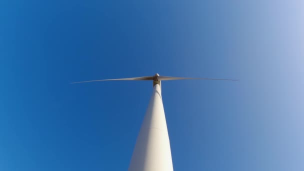 Large wind turbine with blades in the field below view. Blue sky panorama. Windmills farm generating green energy. Sustainable alternative energy. Slow movement. — Stockvideo