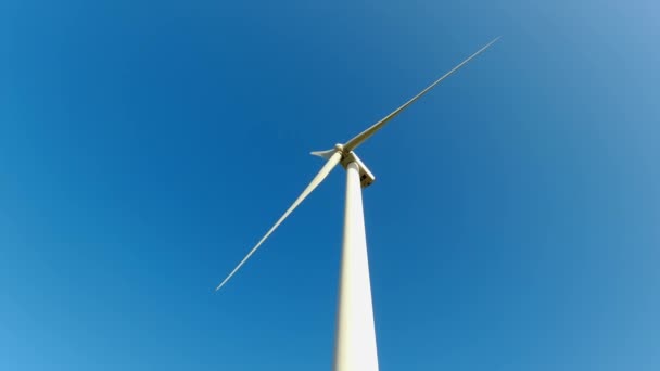 Large wind turbine with blades in the field below view. Blue sky panorama. Windmills farm generating green energy. Sustainable alternative energy. Slow movement. — Vídeo de stock