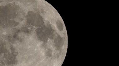 Karanlık gökyüzü arka planında dolunay, Dünya yüzeyinden uzun telefoto lensleriyle çekilmiş. Gri beyaz ay açık gökyüzünde parlıyor.