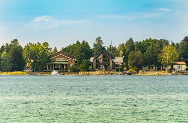 Pike Körfezi 'ndeki Huron Gölü kıyısındaki kır evleri, yaz günü ormanla çevrili. Mevsimlik tatil kiraları ve kişisel boş zaman evleri.  