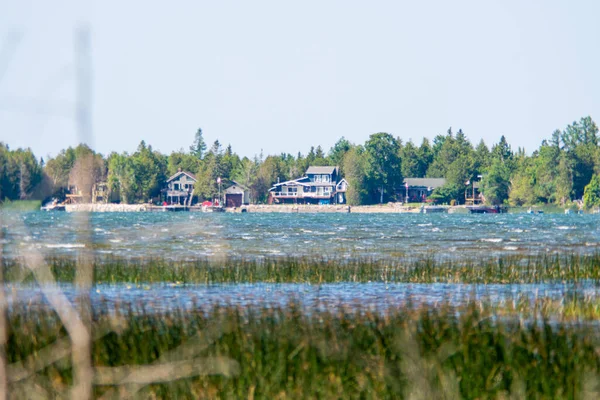 Long distance and very hot summer air make jelly effect at landscape with houses and trees on the shore, water and blue sky. Cottages cabins and fishing lodges for rent and private seasonal leisure.