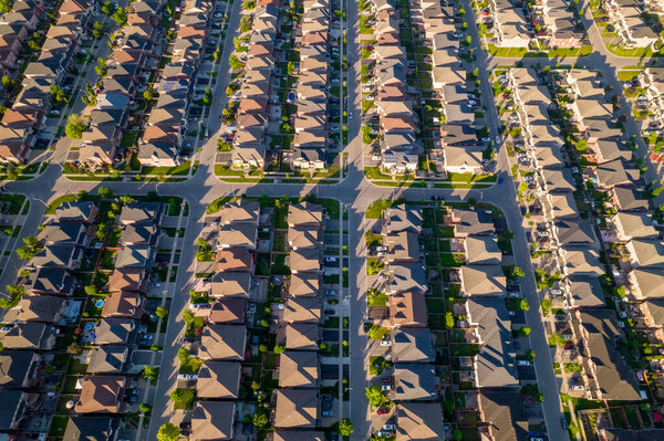 Aerial view of luxury wealthy style and clean single family homes in America with parking space for cars and large green backyards. Golden Hour evening and houses in very geometrical setting pattern.