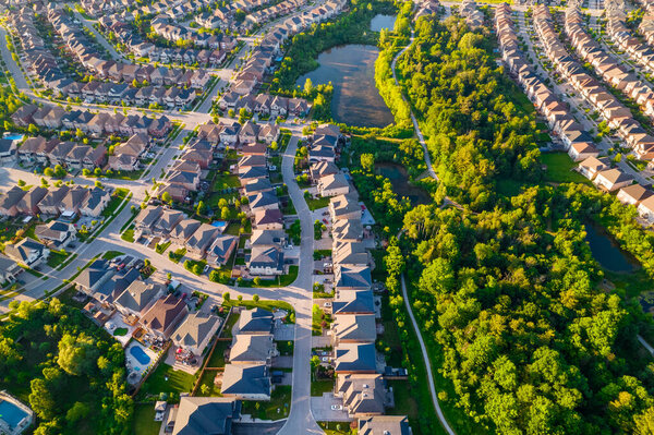 Aerial view of luxury wealthy style and clean single family homes in America with parking space for cars and large green backyards. Golden Hour evening and houses in very geometrical setting pattern.