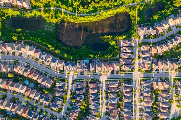 Aerial view of rich American citizens suburb at golden hour summer time. Established Real estate view of wealthy residential houses near greenery, parks and trees.