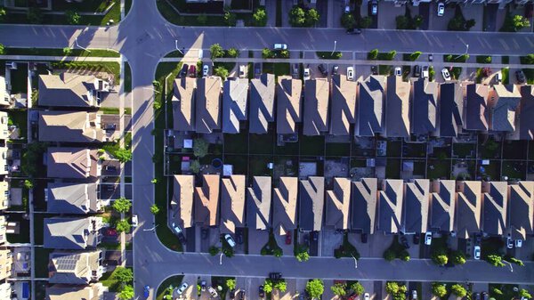 Aerial footage of Canadian town showing suburban housing estates in geometrical position and rows of houses. Summer golden hour evening with long shadows.