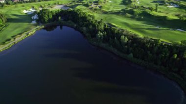 Gökyüzünden golf sahasının kuş bakışı görüntüsü. Akşamları ormanın ve golf sahasının hava görüntüleri. Park ormanı ve golf sahası, yeşil golf sahası üzerinde peyzaj uçuşu..