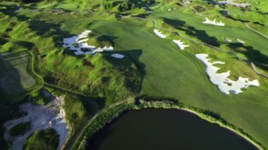 Gökyüzünden golf sahasının kuş bakışı görüntüsü. Akşamları ormanın ve golf sahasının hava görüntüleri. Park ormanı ve golf sahası, yeşil golf sahası üzerinde peyzaj uçuşu..