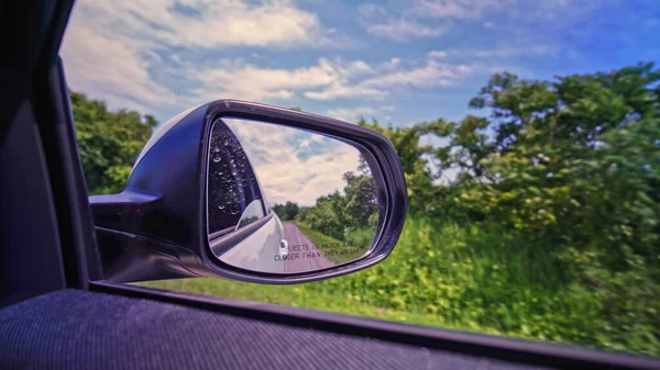 View in the side mirror of a car while driving at rural country side bumpy road. Back view side vehicle mirror look of the passenger. Travel and trip. Drivers license lessons and education. Test drive