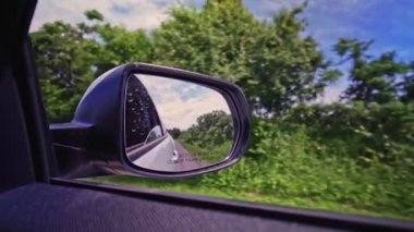Kırsal kesimdeki engebeli yolda giderken arabanın dikiz aynasına bakın. Yolcunun dikiz aynasından görüntüsü. Seyahat ve seyahat. Ehliyet dersleri ve eğitim. Test sürücüsü