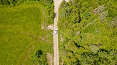 Yeşil ormanın kırsal kesiminde yazın ağaçlarla birlikte yolun dışına çıkan arabanın üzerindeki hava aracı. Vahşi doğada tek arabalı Dağ Ormanı Yolu. Macera ve tatil.