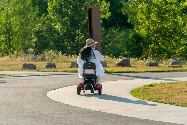 Woman with a disability in the wheelchair mobility scooter enjoying summer park in the evening. Carefree woman with mobility issue uses electric three wheel wheelchair scooter having fun.