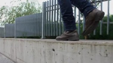 Bir adamın bacaklarının yakın çekimi, kot pantolon ve kahverengi ayakkabılar giyiyor, yolda yürüyor, kamera yan görüş, beton bir patika boyunca yürüyor