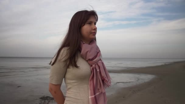 一个穿着浅色夹克和红色围巾的正宗女人的画像 背景是海景 聚精会神 在海滩上放松的概念 — 图库视频影像
