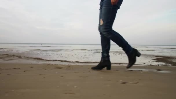 青いジーンズと黒い靴に身を包んだ彼女はバルト海の湾を背景に海沿いのビーチを歩く — ストック動画
