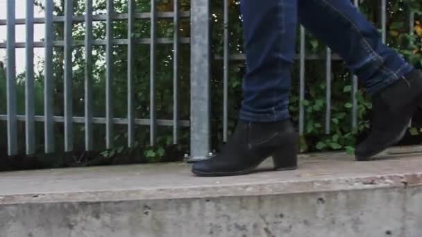 女性腿的特写 穿着蓝色的牛仔裤和黑色的鞋子 她走在路上 侧视相机 走在水泥路上 — 图库视频影像