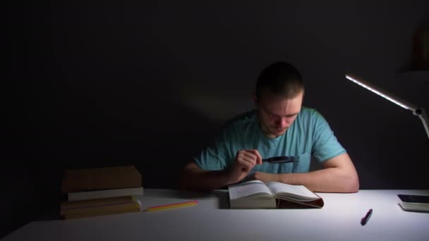Ένας Νεαρός Κάθεται Ένα Τραπέζι Στο Χαμηλό Φως Και Διαβάζει — Αρχείο Βίντεο