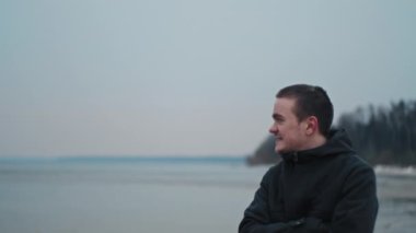 Genç adam deniz yüzeyindeki mesafeye bakıyor, üzgün ve soğuk.