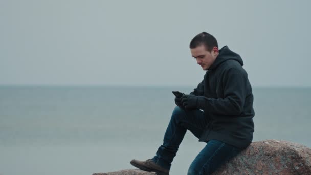 Jovem Está Sentado Uma Pedra Contra Fundo Mar Azul — Vídeo de Stock