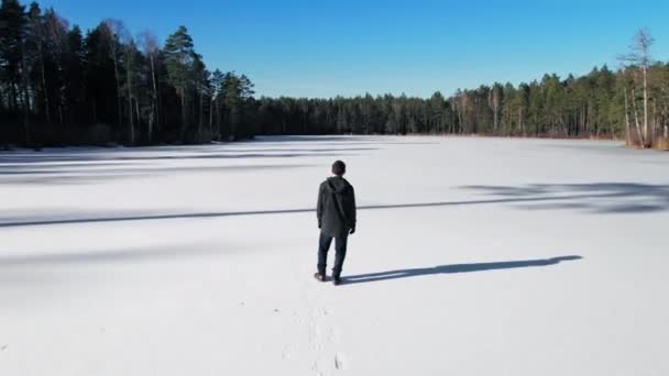 一个穿着深色衣服 留着短发的年轻人走在冰冷的湖面上 具有电影全景相机运动的空中镜头 — 图库视频影像