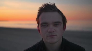 Bir adam gün batımında kameraya bakar ve gün batımında Jurmala kumsalının arkasında gülümser.