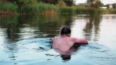 A young guy in swimming goggles dives and swims in a pond, this is a dolomite quarry filled with water, a man swims and rests