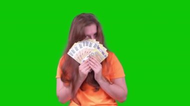 A Young Woman In An Orange T-Shirt With Money Looks Into The Camera On A Green Screen. High quality 4k footage