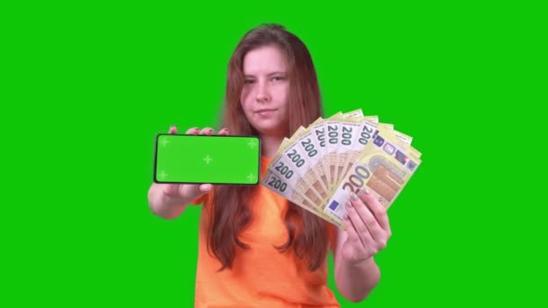 Young Woman Orange Shirt Money Phone Looks Camera Green Screen — 비디오