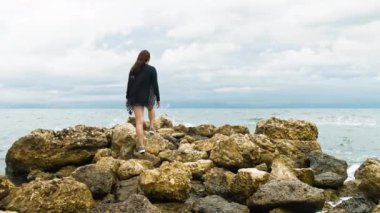 Kayaların üzerinde duran yakışıklı kadın ellerini kaldırır ve denize bakar. Yüksek kalite 4k görüntü