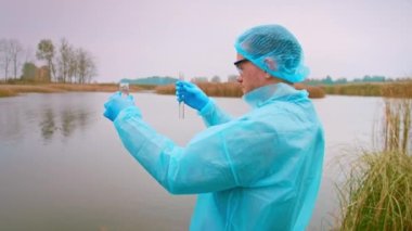 Araştırmacı suyun kalitesini kontrol ediyor. Koruyucu Takım Elbiseli Bilim Adamı deney tüpünden şişeye su döker. Enfeksiyon testi, zararlı emisyonlar. Yüksek kalite 4k görüntü