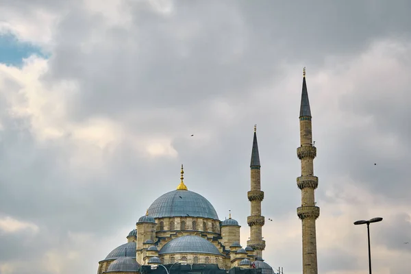 A huge ottoman empire mosque of yeni mosque (yeni camii) under cloudscape day and overcast weather in istanbul with electricity post and street lights